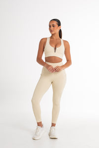 Full-body shot of a woman in a cream sports bra and high-waisted leggings. The activewear set highlights a sleek, body-contouring fit with side pockets, perfect for versatile and stylish movement.