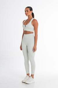Full-body shot of a woman in a mint sports bra and high-waisted leggings. The activewear set highlights a sleek, body-contouring fit with side pockets, perfect for versatile and stylish movement.