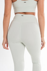 Back view of a woman wearing a matching light mint ice activewear set, including a high-waisted leggings and a fitted sports bra. The leggings feature side pockets and a smooth, contouring design that enhances the body’s natural shape. The background is a clean, minimalistic white, highlighting the sleek, seamless look of the activewear.