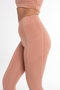 Close-up of a woman wearing a fawn sports bra and high-waisted leggings, showcasing a sculpted fit with side pockets and a seamless, breathable design. Ideal for active and versatile wear.