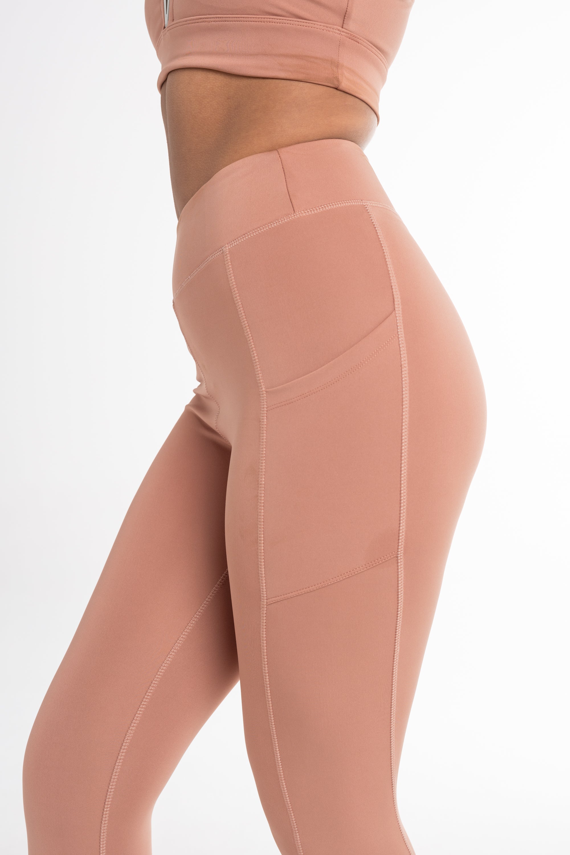 Close-up of a woman wearing a fawn sports bra and high-waisted leggings, showcasing a sculpted fit with side pockets and a seamless, breathable design. Ideal for active and versatile wear.