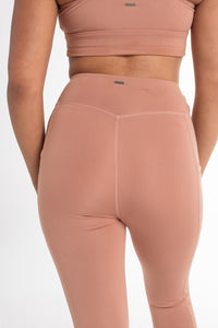 Back view of a woman wearing a fawn sports bra and high-waisted leggings with a sculpted fit. The set features a minimalist design and seamless fabric for comfortable movement.