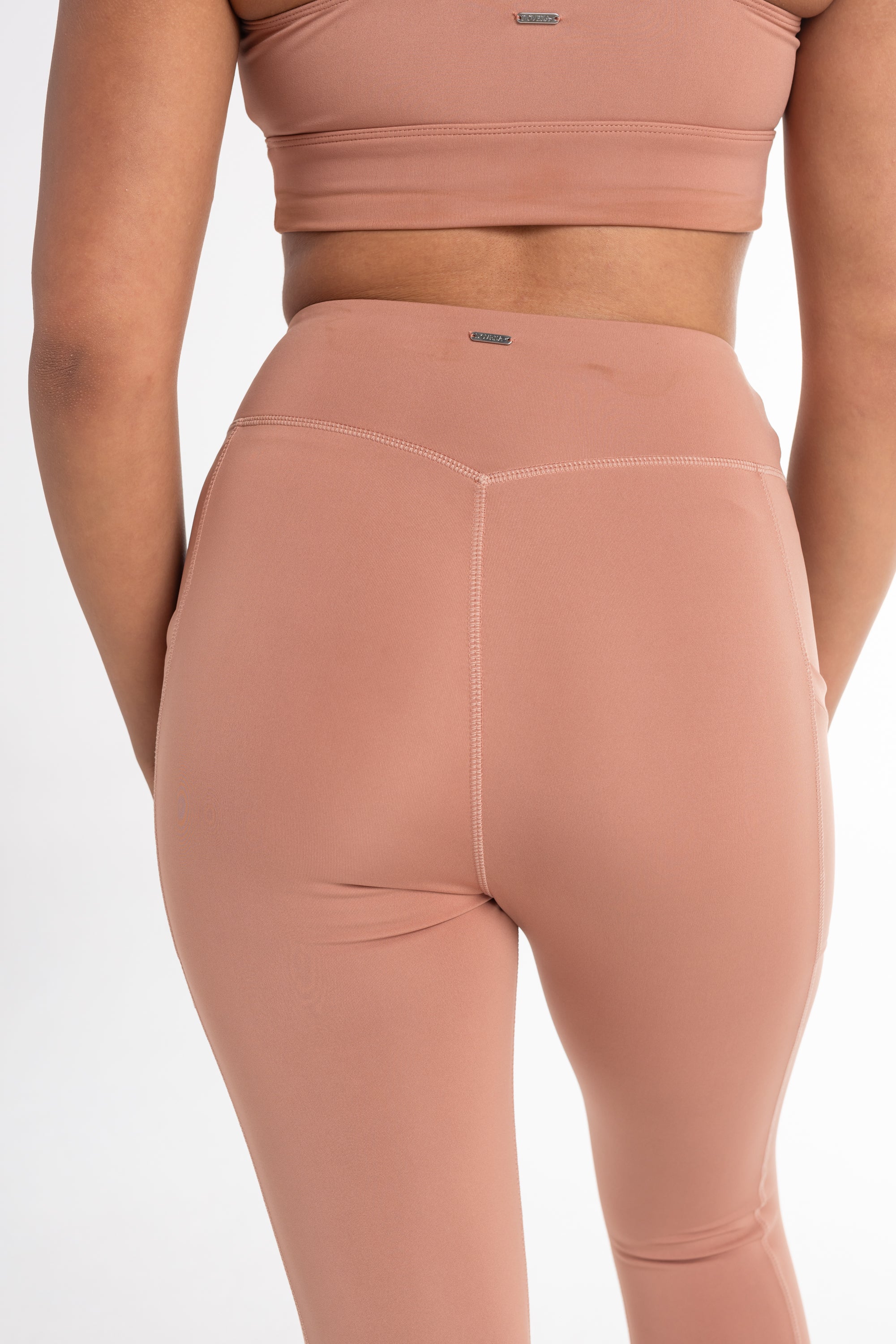 Back view of a woman wearing a fawn sports bra and high-waisted leggings with a sculpted fit. The set features a minimalist design and seamless fabric for comfortable movement.