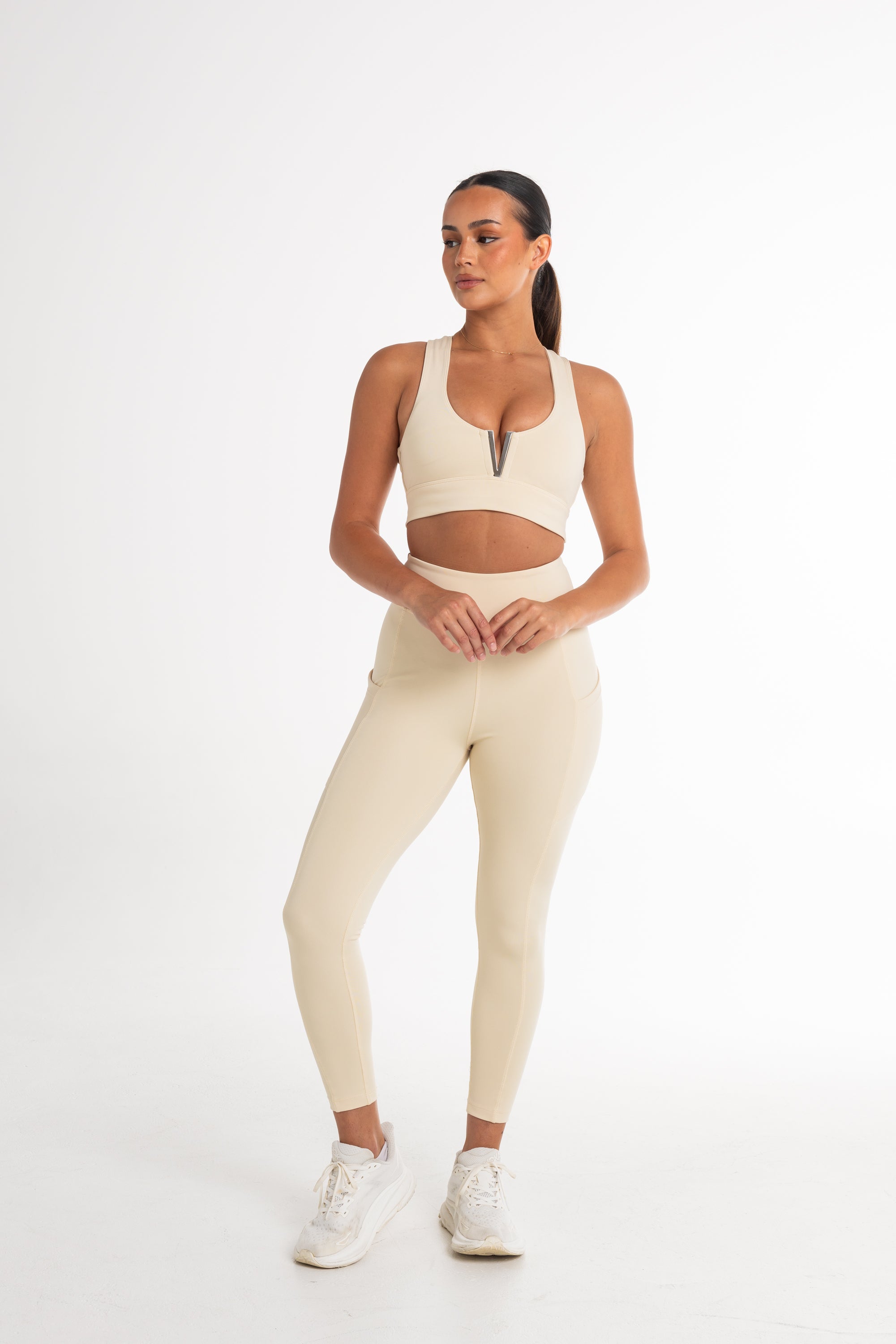 Full-body shot of a woman in a cream sports bra and high-waisted leggings. The activewear set highlights a sleek, body-contouring fit with side pockets, perfect for versatile and stylish movement.