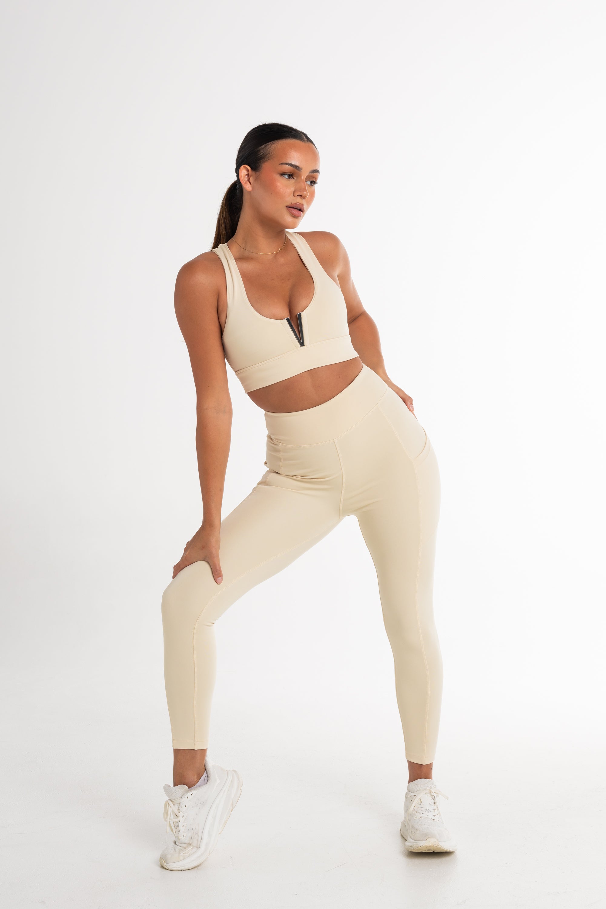 Full-body shot of a woman in a cream sports bra and high-waisted leggings. The activewear set highlights a sleek, body-contouring fit with side pockets, perfect for versatile and stylish movement.