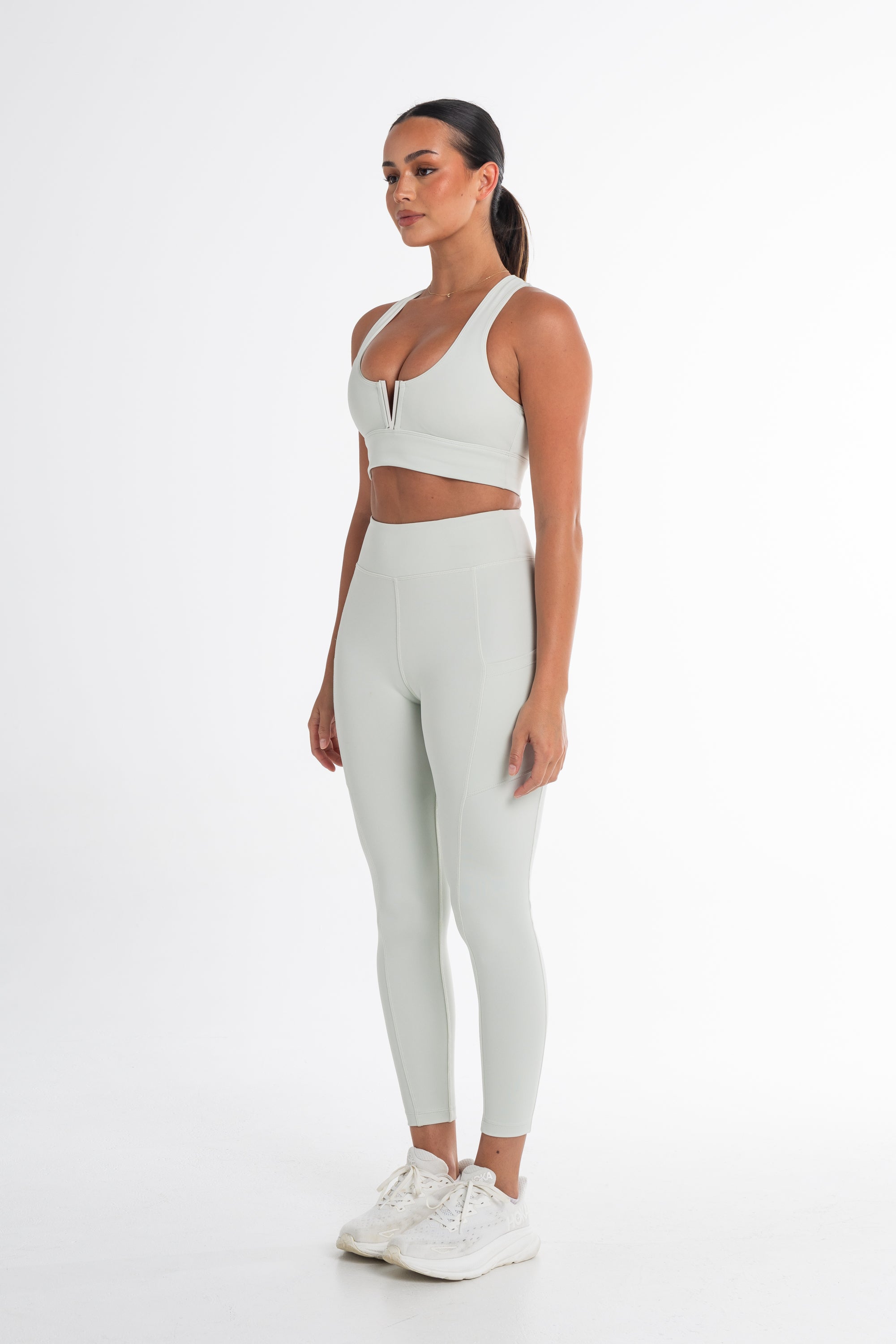 Full-body shot of a woman in a mint sports bra and high-waisted leggings. The activewear set highlights a sleek, body-contouring fit with side pockets, perfect for versatile and stylish movement.
