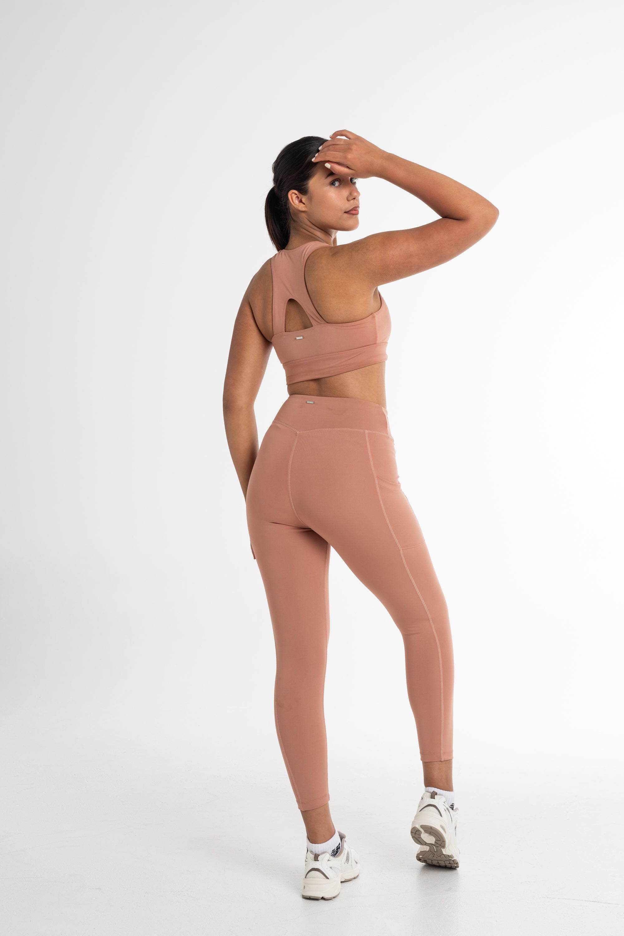 Full-body shot of a woman in a fawn sports bra and high-waisted leggings. The activewear set highlights a sleek, body-contouring fit with side pockets, perfect for versatile and stylish movement.