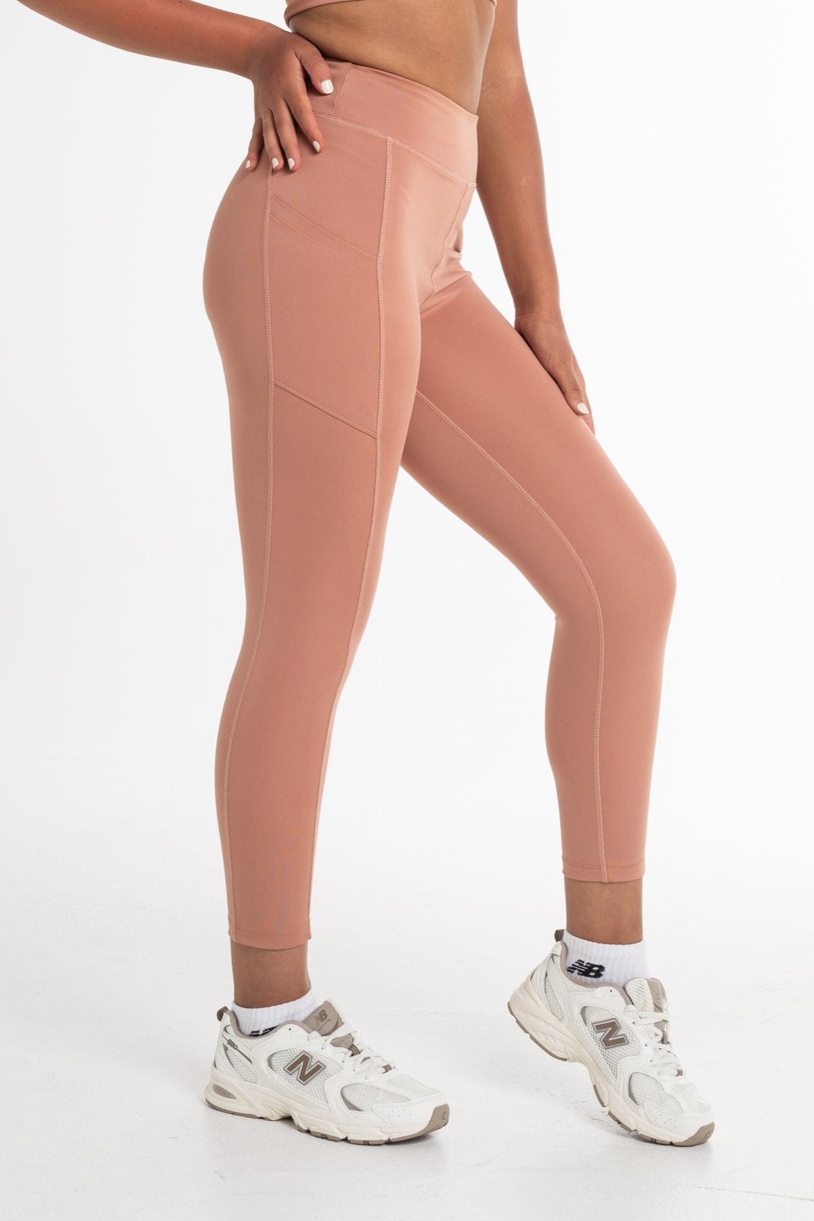 Close-up of a woman wearing a fawn sports bra and high-waisted leggings, showcasing a sculpted fit with side pockets and a seamless, breathable design. Ideal for active and versatile wear.