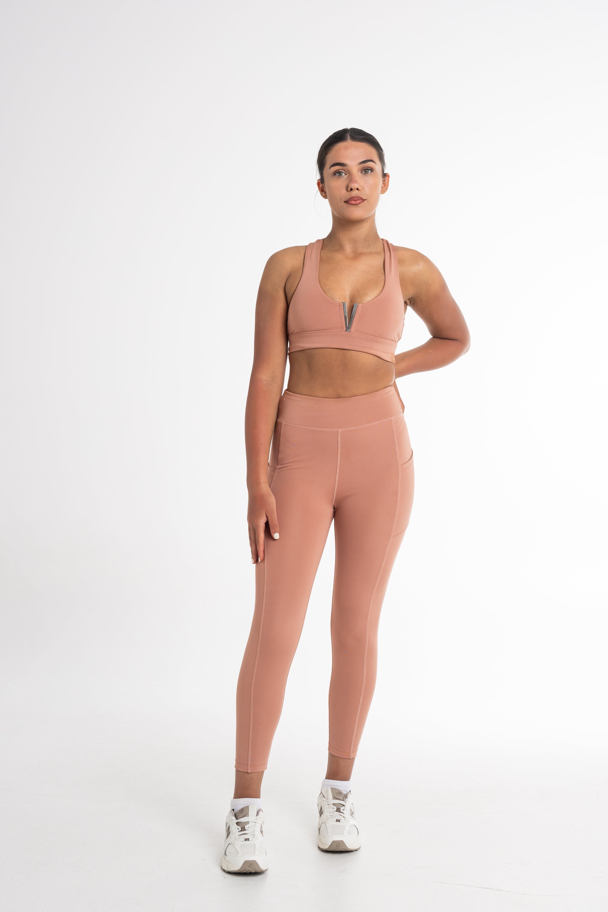 Full-body shot of a woman in a fawn sports bra and high-waisted leggings. The activewear set highlights a sleek, body-contouring fit with side pockets, perfect for versatile and stylish movement.